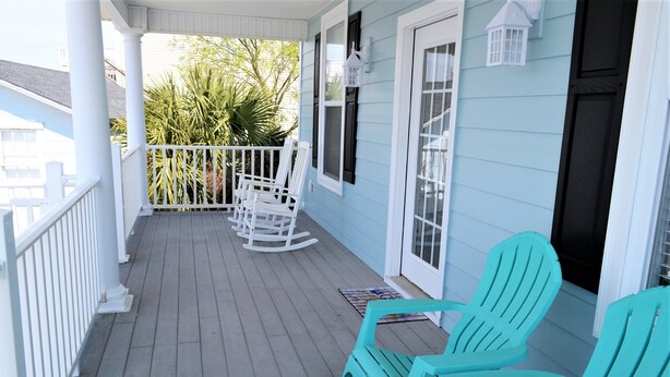 Een veranda met witte reling, turquoise Adirondack-stoelen en een witte schommelstoel.