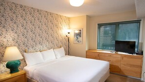 Une chambre à coucher bien rangée, avec un lit, une table de chevet, une lampe, une commode et un téléviseur posé sur la commode.