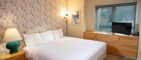 Un dormitorio ordenado con cama, mesita de noche, lámpara, cómoda y un televisor sobre la cómoda.