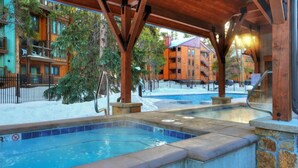 Un espace piscine agrémenté d’une pergola en bois, d’un jacuzzi et offrant une vue sur un immeuble à plusieurs étages doté de balcons.