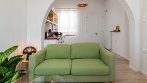 Un salon avec un canapé vert, une table basse en verre et une plante en pot.