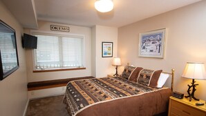 A bedroom with a large bed, a window with blinds, a bedside table with a lamp, and a wall-mounted TV. - Condo with Ski-in/Ski-Out Access, Pools and More! (Ludlow)