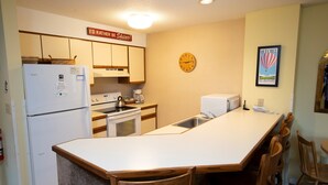 A kitchen with a refrigerator, stove, sink, and wooden chairs. - Condo with Ski-in/Ski-Out Access, Pools and More! (Ludlow)