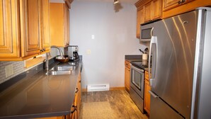 A kitchen with wooden cabinets, stainless steel appliances, a microwave, and a built-in oven. - Charming + Rustic Condo with Ski-in/Ski-Out Access (Ludlow)