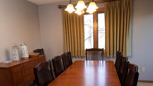 A dining room with a wooden table, chairs, a chandelier, and a window with curtains. - Charming + Rustic Condo with Ski-in/Ski-Out Access (Ludlow)