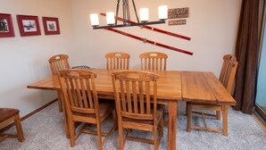 Een eetkamer met een houten tafel, stoelen, een kroonluchter en ingelijste foto's aan de muur.