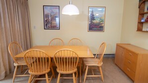 Un coin repas avec une table en bois et six chaises, un luminaire suspendu blanc et deux tableaux encadrés au mur.