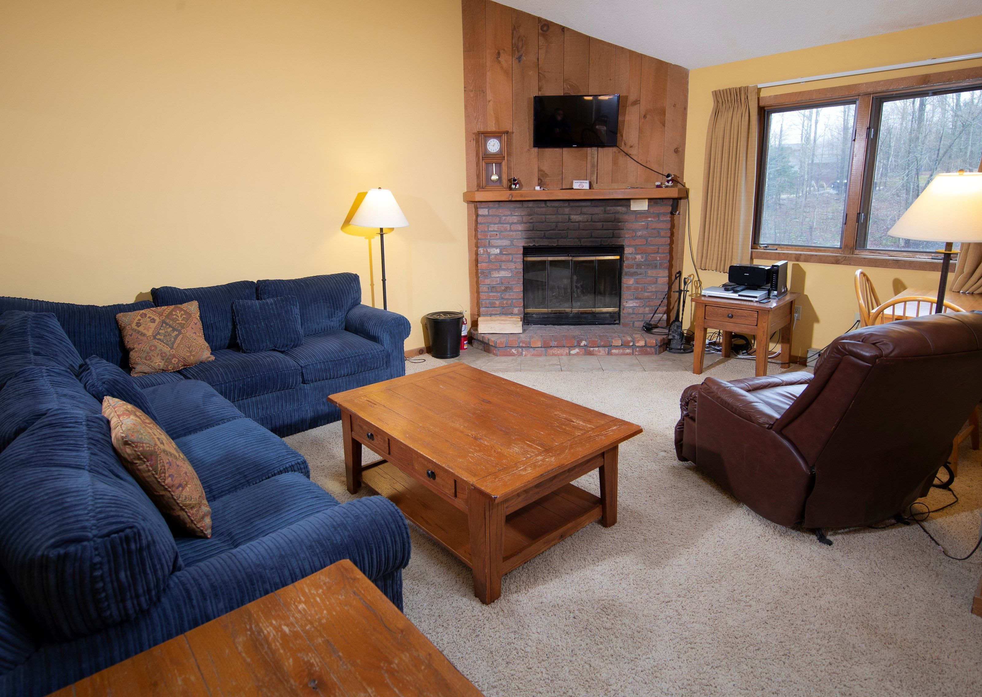 A living room with a blue sofa, a wooden coffee table, a leather armchair, a fireplace, and a television mounted on the wall.