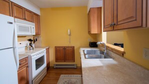 A kitchen with wooden cabinets, a white refrigerator, a microwave, an oven, a sink, and a telephone. - Amazing Location! Charming Ski-in/Ski-out Condo (Ludlow)
