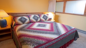 A bedroom with a bed, two bedside lamps, a window with curtains, and a wooden headboard. - Amazing Location! Charming Ski-in/Ski-out Condo (Ludlow)
