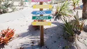 Un cartello in legno con diverse frecce direzionali che indicano varie destinazioni come Spiaggia, Andros, Abaco, Eleuthera, Mayaguana, Exuma, Piscina, Inagua e Osa.