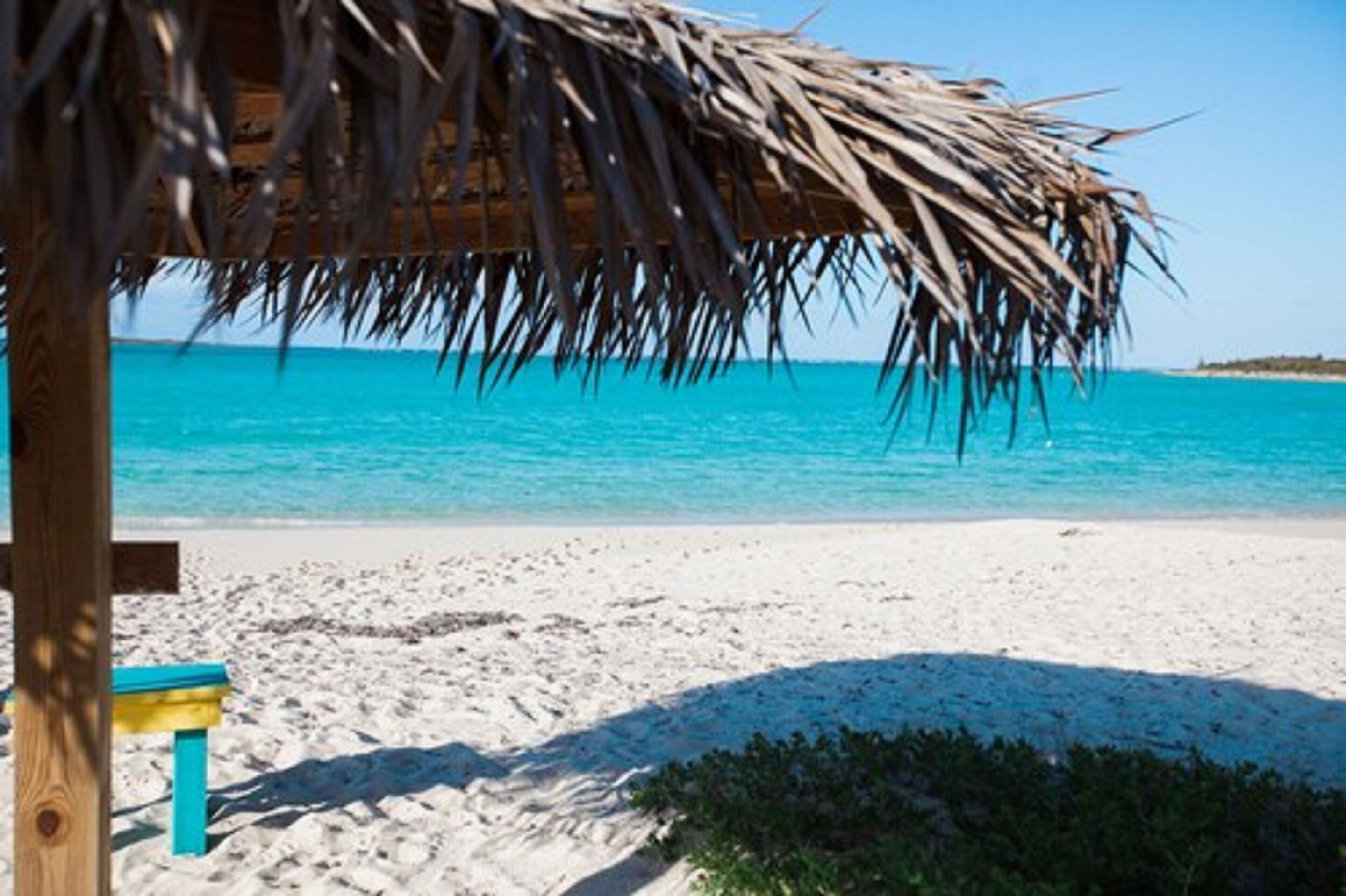 A beach with a thatched roof structure and a bench.