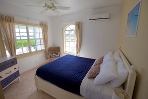 A bedroom with a bed, a dresser, a ceiling fan, and two windows. - Paradise Bay (Rokers Point)