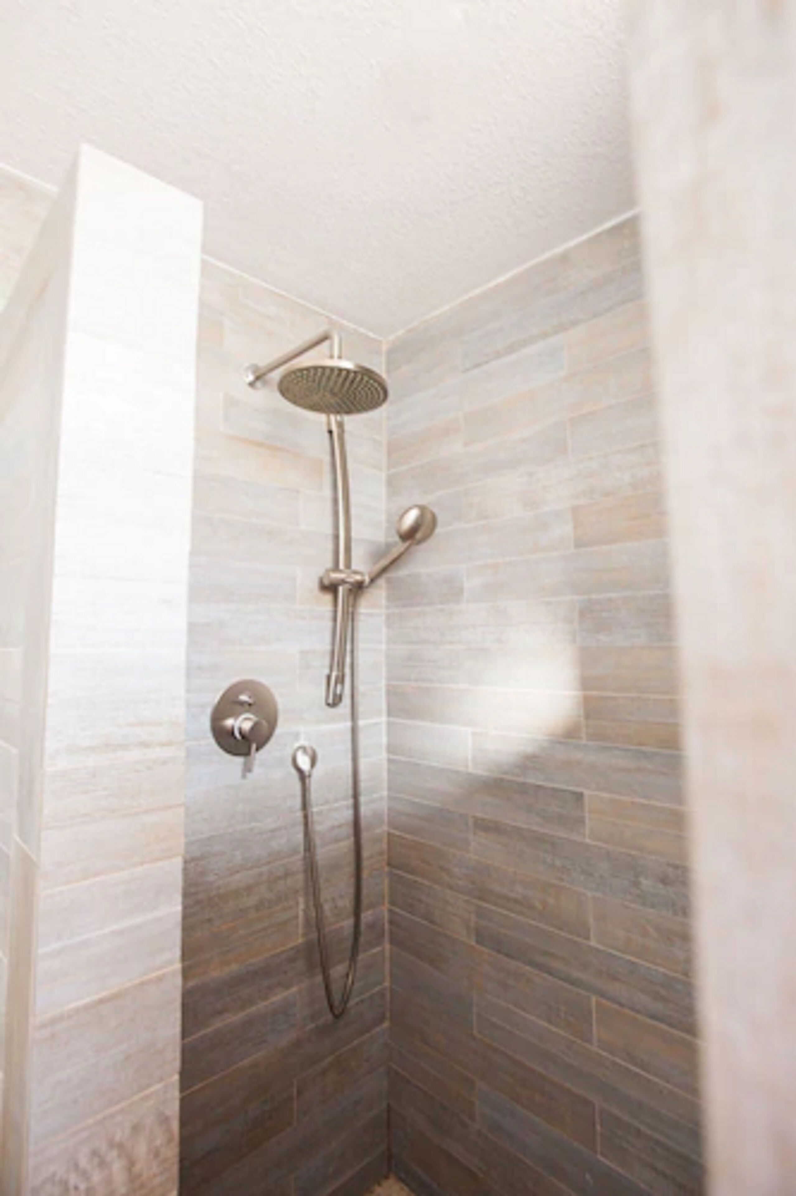 A shower with a handheld showerhead and a wall-mounted control.