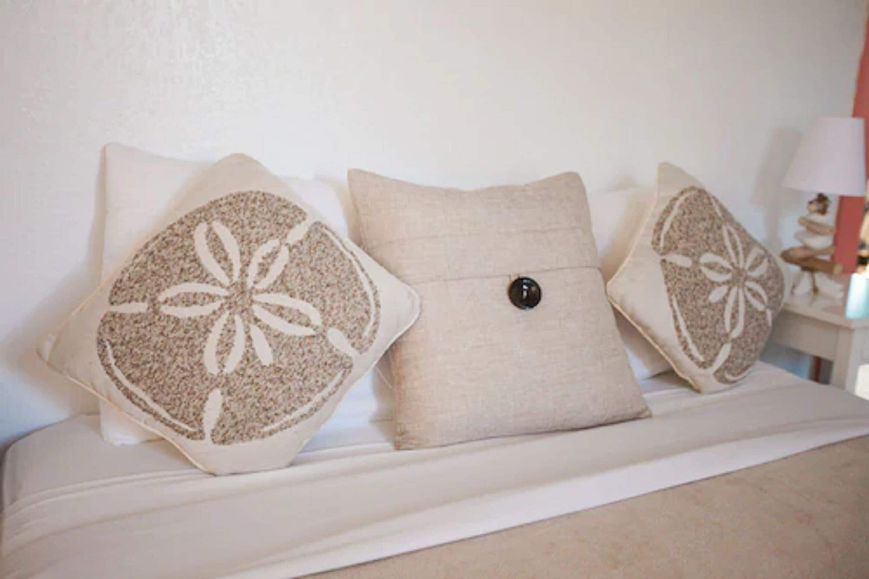 A bed with three pillows, one with a floral pattern and two plain ones.