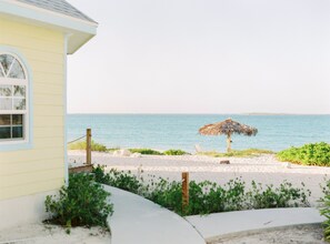 A beach view with a thatched umbrella, a sandy path, and a building with a window. - Paradise Bay (Rokers Point)