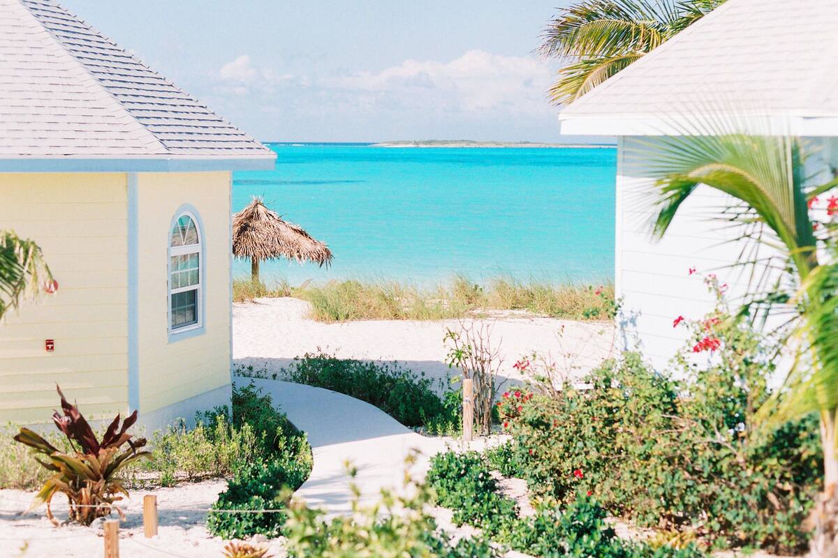 A beachfront property with a thatched-roof structure, a sandy pathway, and lush greenery.