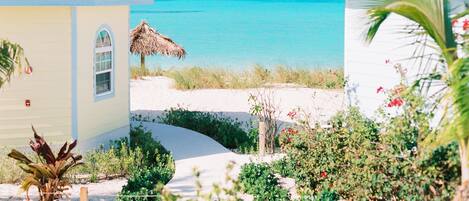 A beachfront property with a thatched-roof structure, a sandy pathway, and lush greenery.
