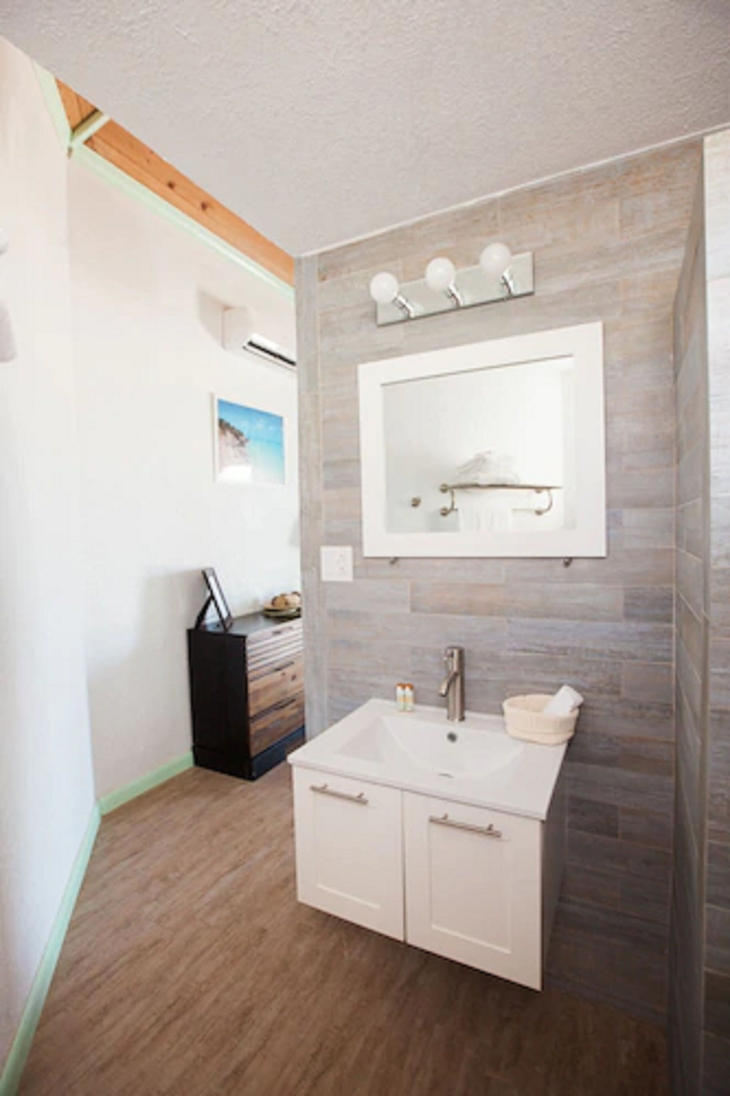 Un bagno con un lavandino bianco, uno specchio e un pavimento in legno.