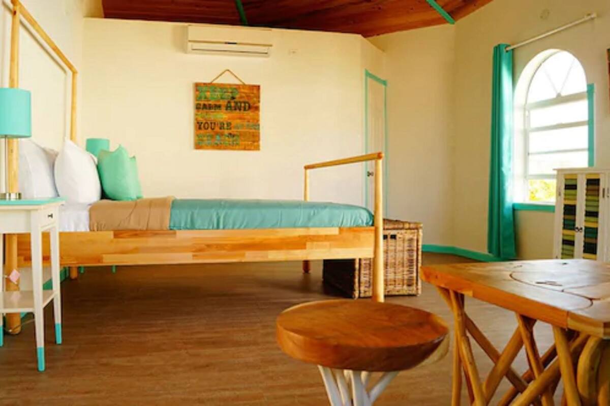 A room with a bed suspended from the ceiling, a small table, a stool, and a wall-mounted air conditioner.
