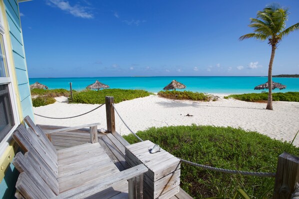 Una terraza de madera que conduce a una playa con sombrillas de paja y una palmera.