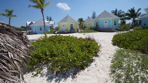 Una proprietà fronte spiaggia con diversi edifici blu e gialli, un sentiero sabbioso e palme.
