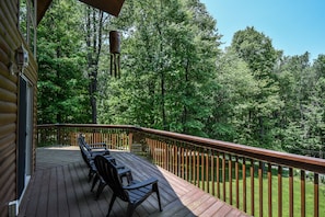 A wooden deck with a railing, surrounded by dense forest. - Howling Wolf Den (Oakland)