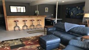 A modern living room with a blue leather sofa, a patterned rug, a bar area with stools, and a painting on the wall.