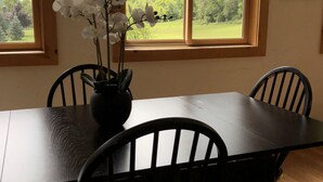 A dining area with a table and chairs, a vase with white flowers, and a view of mountains through a window.