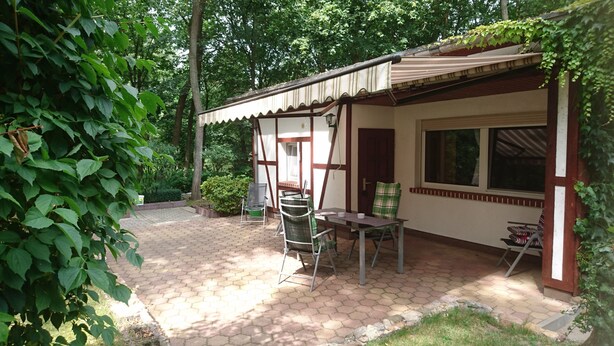 Un patio couvert, agrémenté d’une table et de chaises, et entouré de verdure et d’arbres.