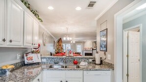 Una cucina con mobili bianchi, piani di lavoro in granito, lavastoviglie integrata e un albero di Natale.