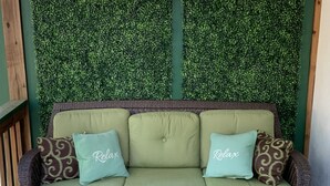 Un divano verde con due cuscini, ognuno con la scritta "Relax", davanti a una parete decorata con un motivo di foglie verdi.