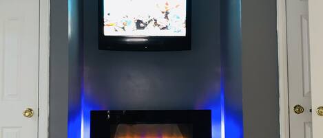 A room with a flat-screen TV mounted above a fireplace with blue LED lighting.