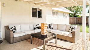 A covered patio area with a wicker sofa set, a black coffee table, and a stack of bricks. - “Spacious 5-Bedroom Retreat – Perfect for Families & Groups” (Citrus Heights)