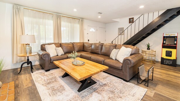 A modern living room with a brown leather sofa, a wooden coffee table, and a staircase. - “Spacious 5-Bedroom Retreat – Perfect for Families & Groups” (Citrus Heights)