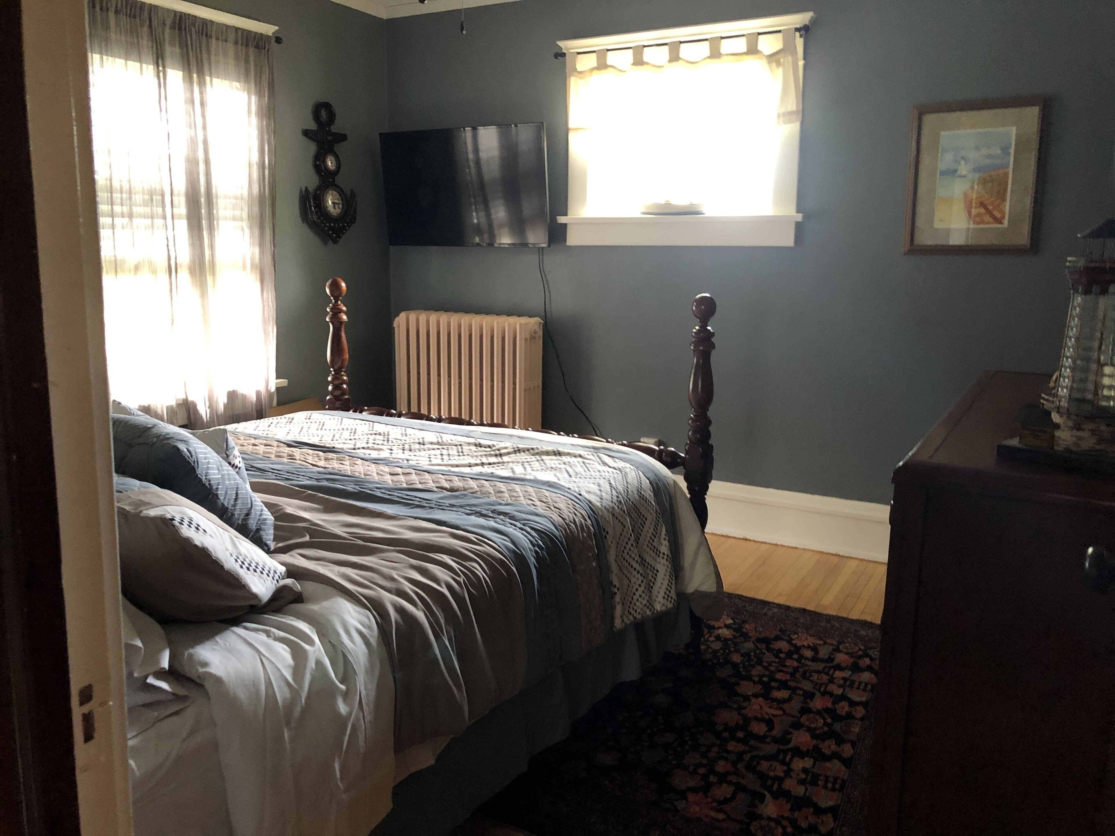 Un dormitorio con cama, un radiador, televisor y ventana con cortinas.