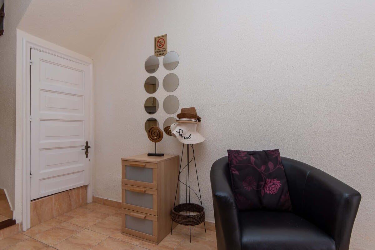 Ein Zimmer mit einer weißen Tür, einem Holzschrank, einem schwarzen Ledersessel und einer wandmontierten Spiegelanordnung.