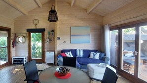 A cozy cabin interior with a dining area, a sofa, a kitchen, and large windows.