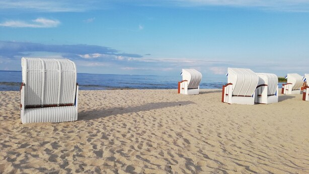 A beach with white beach chairs and umbrellas, arranged in rows.
