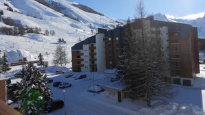 A snow-covered mountain resort with a multi-story building, ski slopes, and parked cars.