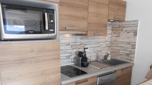 A modern kitchen with a built-in microwave, a coffee maker, a dishwasher, and a stone backsplash.