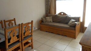 A room with a wooden dining table and chairs, a sofa with cushions, and a window with curtains.