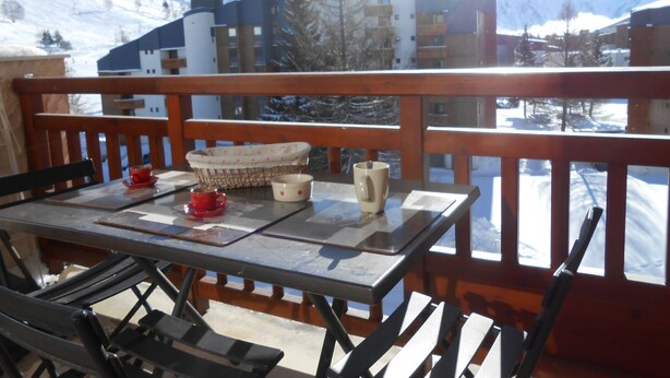 A balcony with a table set for two, overlooking a snowy mountain landscape and buildings.