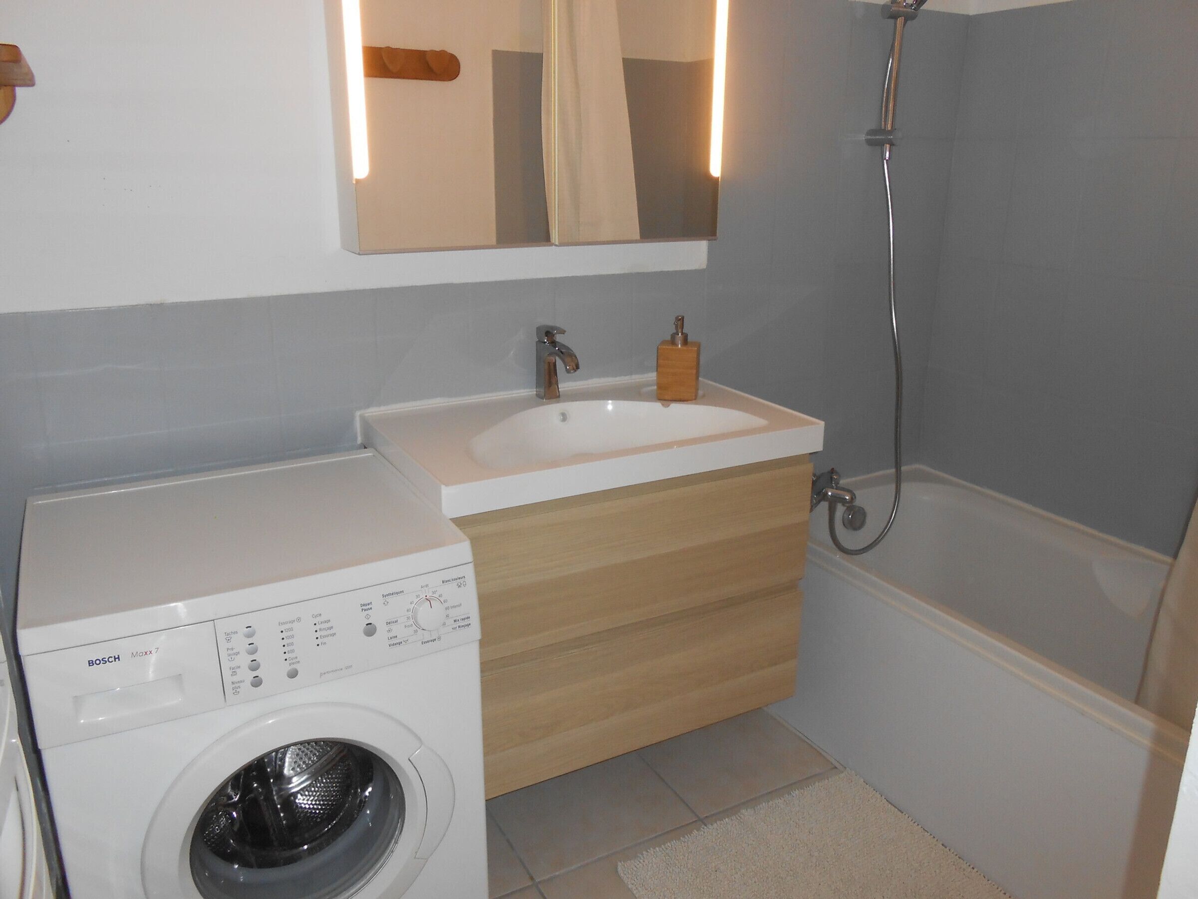 Ein kleines Badezimmer mit Waschmaschine, Waschbecken und Dusche.