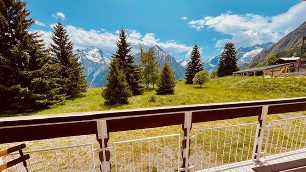 A balcony with a view of a mountain range, wooden benches, and a railing.