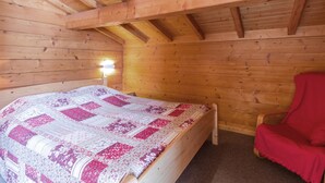 Une pièce chaleureuse, aménagée dans un chalet en bois, avec un lit, une table de chevet et un fauteuil rouge.