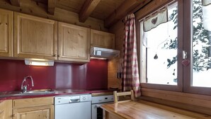 A wooden cabin kitchen with a red countertop, wooden cabinets, a white dishwasher, and a window with a plaid curtain. - Cozy chalet for 10, fireplace, garage, WIFI, pets welcome (La Clusaz)