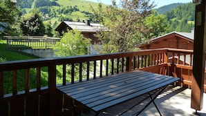 A wooden deck with a bench, overlooking a mountainous landscape with houses and greenery. - Cozy chalet for 10, fireplace, garage, WIFI, pets welcome (La Clusaz)