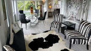 Ein geräumiges Wohnzimmer mit hoher Decke, einem Glastisch, schwarz-weiß gestreiften Sofas und einem großen schwarzen und weißen Kuhfellteppich.
