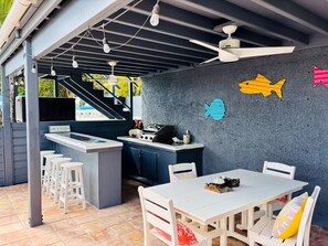 Un espace cuisine extérieur comprenant un barbecue, des tabourets de bar et une table à manger avec des chaises.